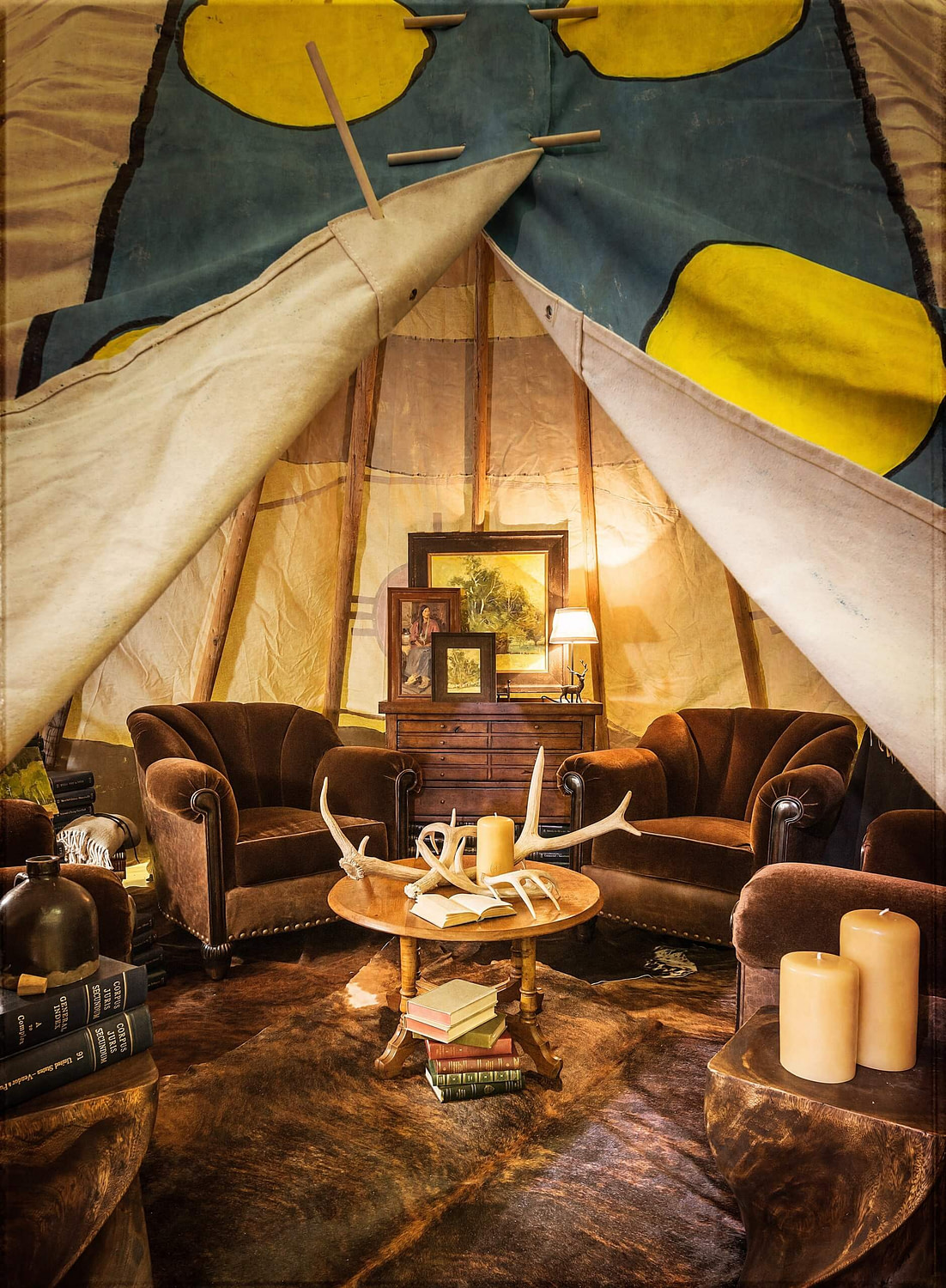 Inside of tipi with two brown mohair armchairs, hair on hide rug, Santa Rosa Candles, antlers on center table