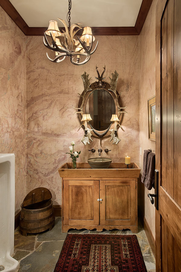 Bathroom with bowl sink on wood 2 door cabinet, oval mirror with antlers accent. Antler chandelier in center of room.