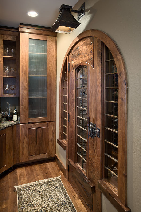 Handcrafted wood wine room door in Greene &amp; Greene-style with inset glass and hand-forged hardware