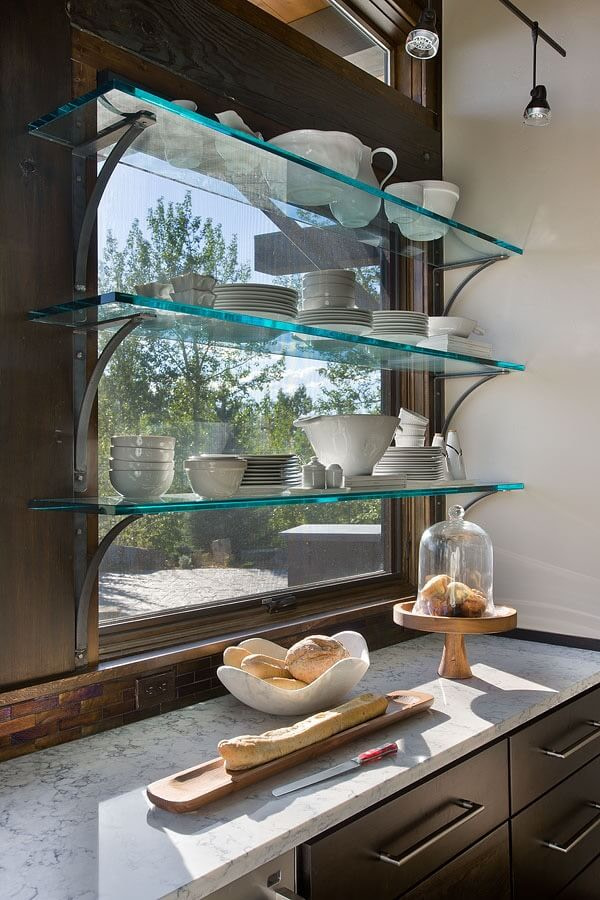 3 glass shelves across kitchen window holding white plates and dishes.